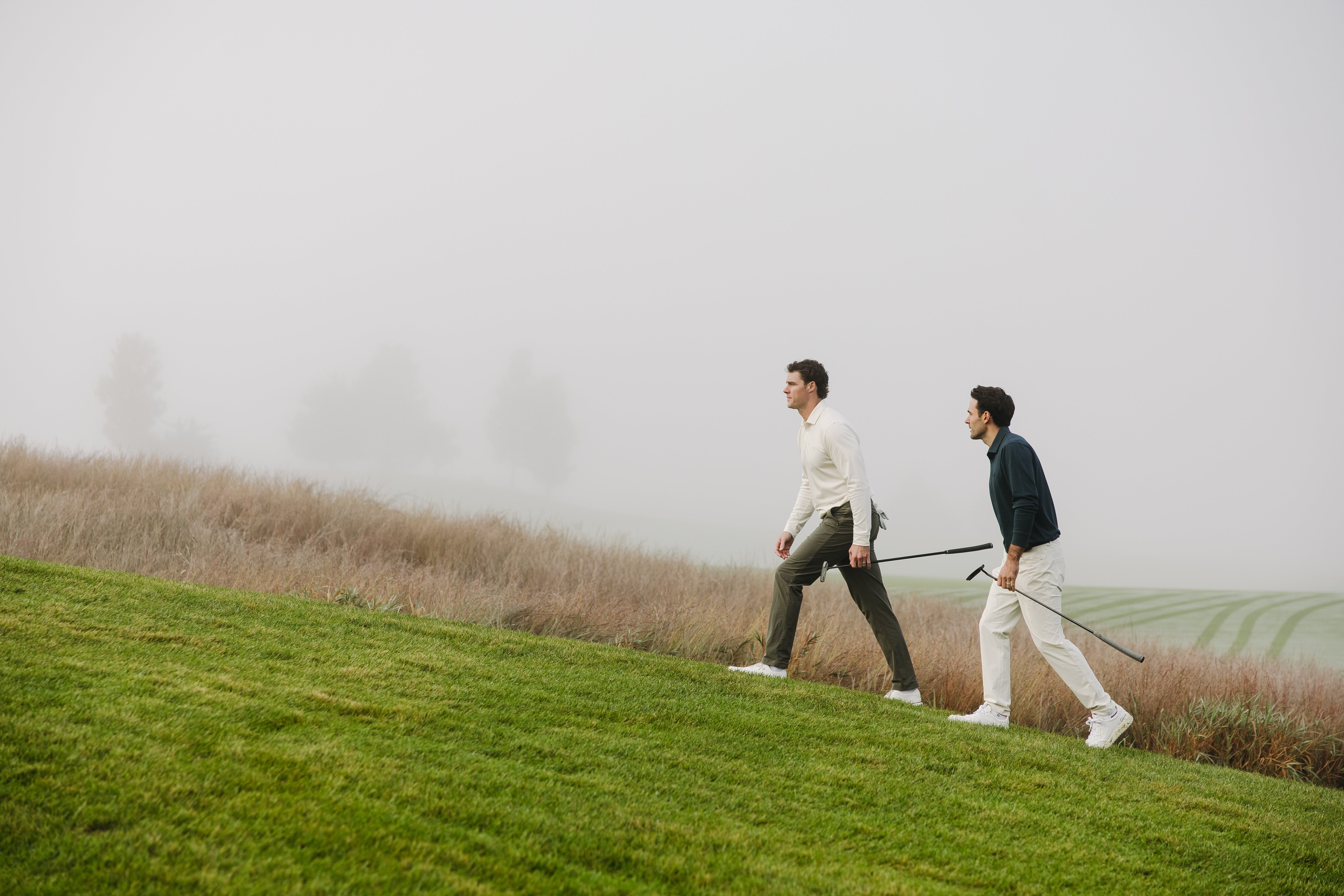 Two men walking on a grassy field with a misty background - Olydoe Golf