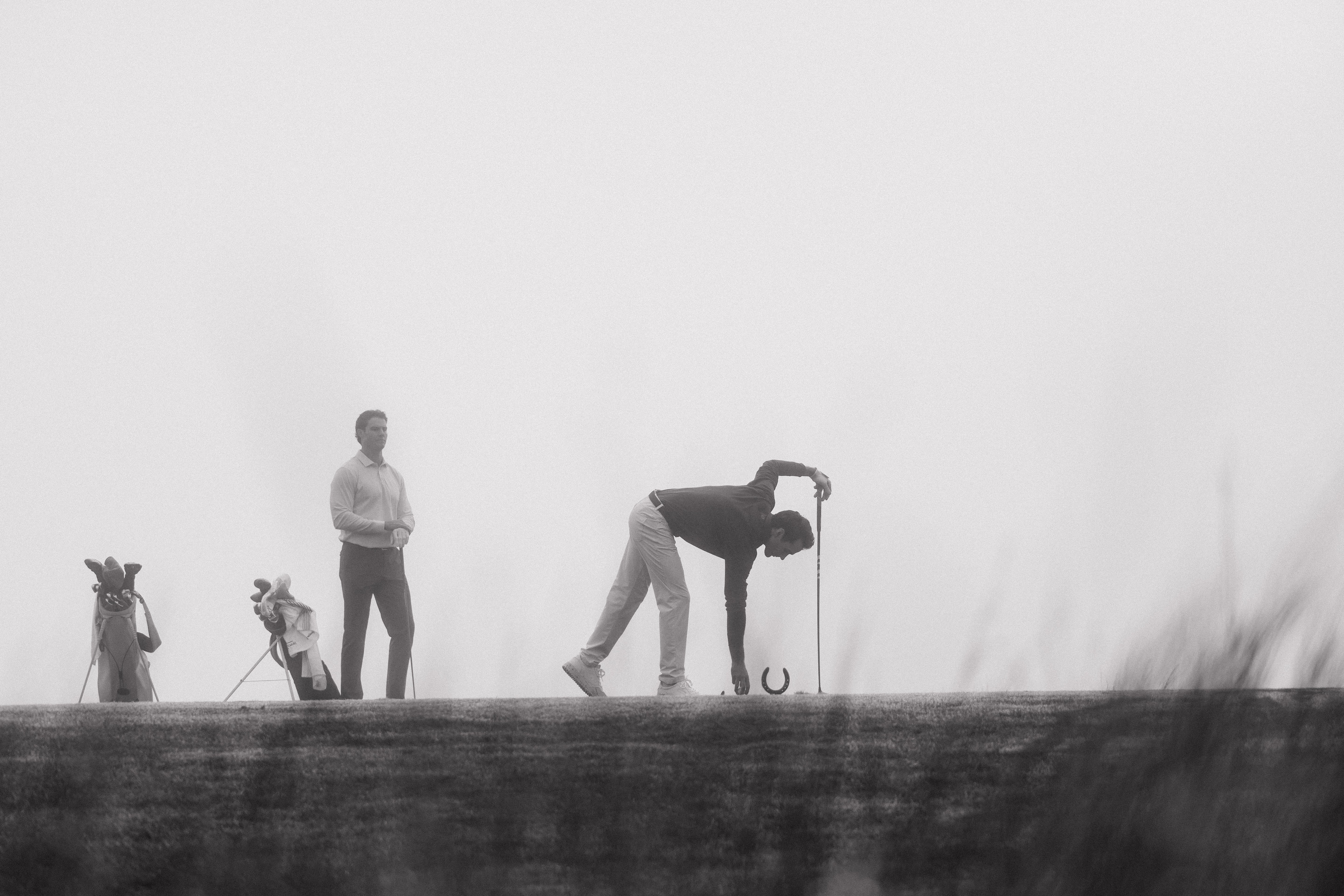 Golfers on a foggy golf course with one player in action and others observing. Olydoe Golf